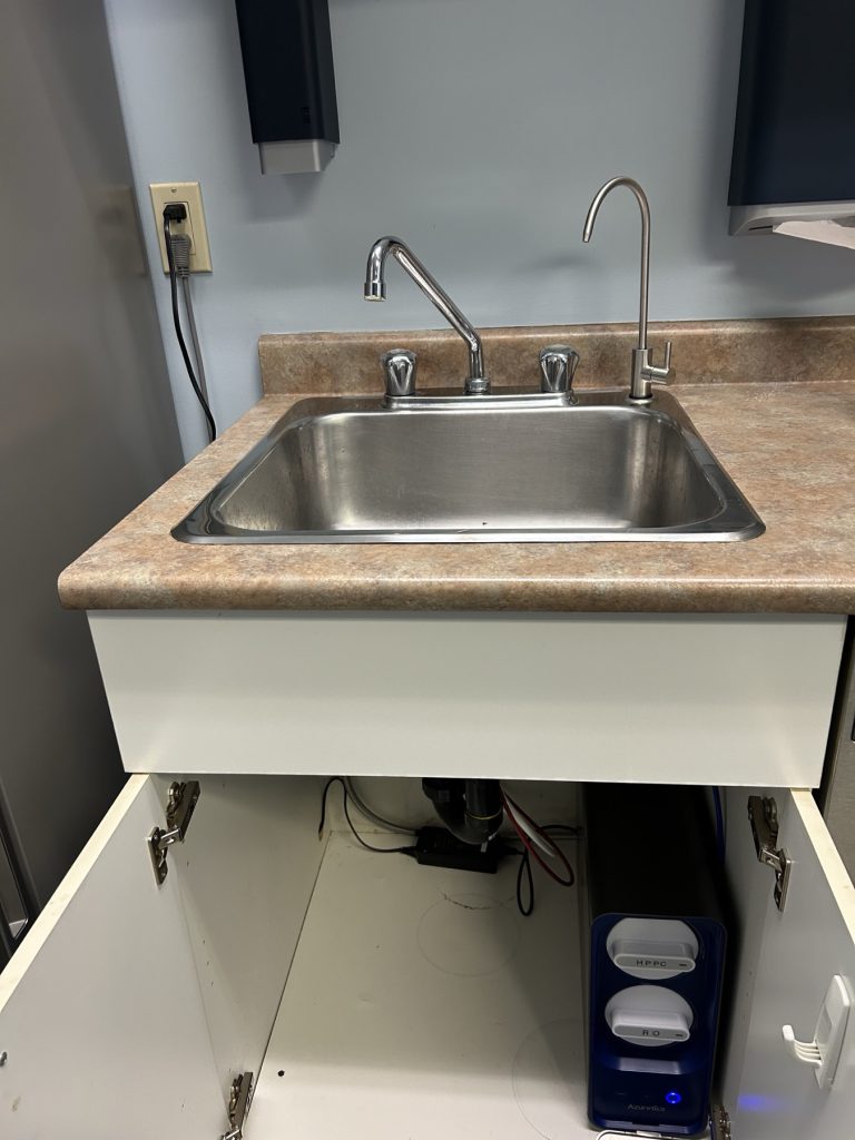 Kitchen sink with a dedicated RO dispensing faucet and the Azuretics tankless reverse osmosis unit visible in the open cabinet below